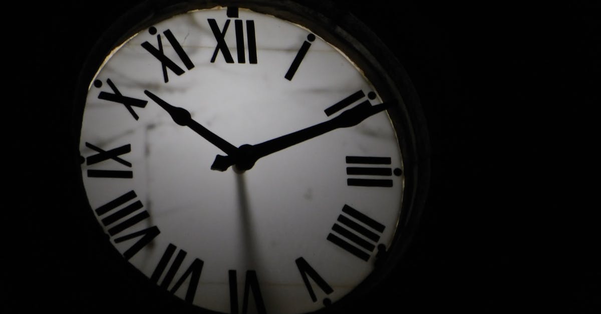 Flight compensation due to a delay in the second leg only - Round mechanical clock with black arrows and numbers on white face ticking on black background in darkness