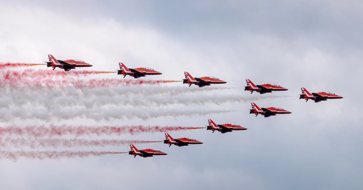 Flight deals from the UK - Low angle of modern red military aircraft flying in cloudy sky symmetrically and creating lines with color smokes during air show
