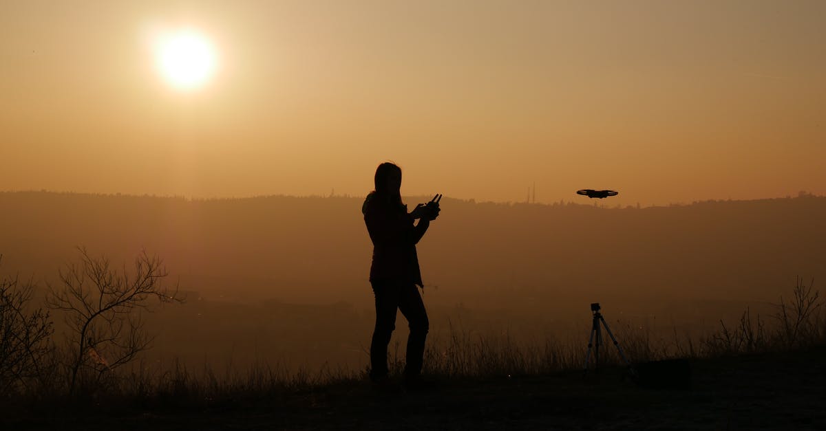 Flight fares and distance of the travel [duplicate] - Full body silhouette of anonymous person standing on slope at sunset and using remote control for operating drone