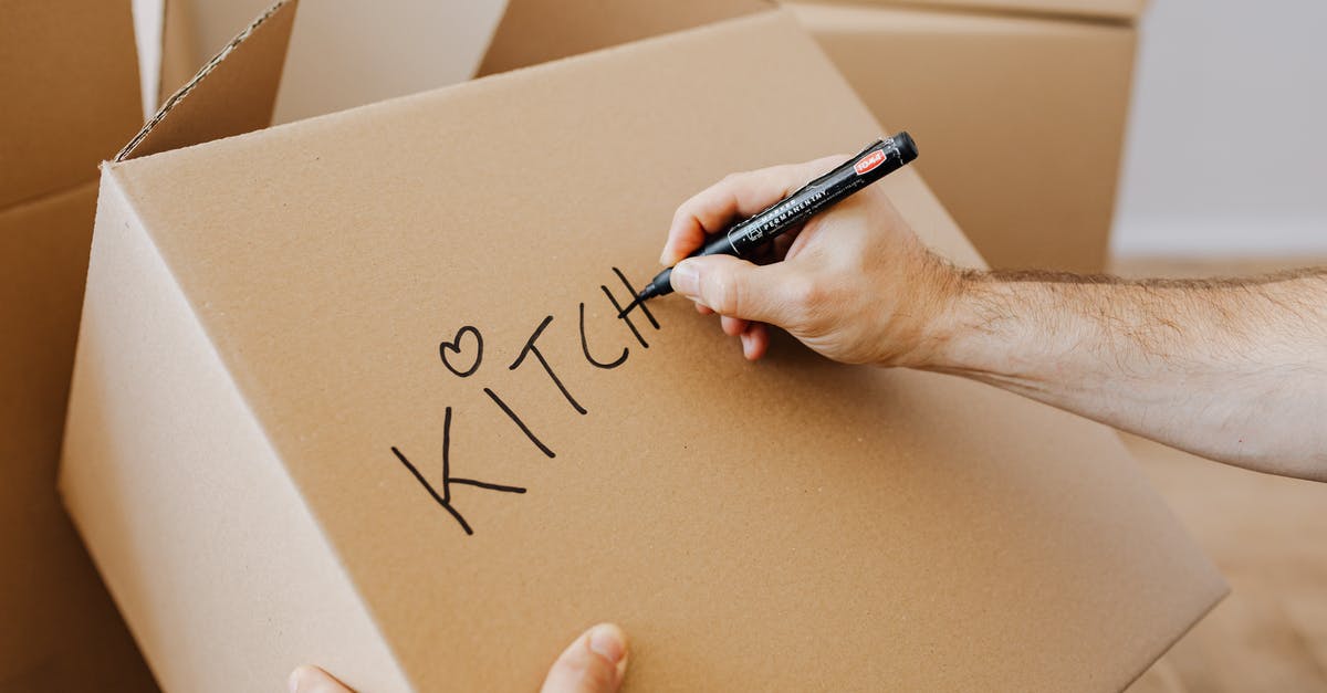 Flight itinerary/time/date change - From above of unrecognizable adult male writing with black marker on cardboard containers while packing staff and preparing for relocation in new home