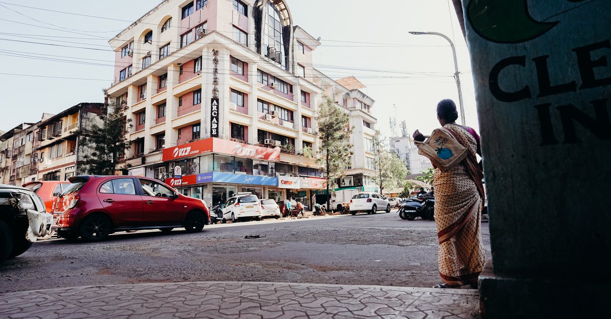 Flying from Halifax via London to India and back from Jeddah - Man in Brown Jacket Standing on Sidewalk Near Cars and Buildings