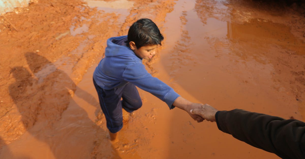 Flying in and out of Copenhagen. Do I need to go through security? - High angle of crop person holding hands with ethnic boy stuck in dirty puddle in poor village