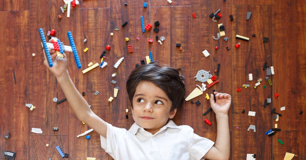 Flying on the 2nd floor of the airplane [closed] - Top view of concentrated kid lying on floor among various details of construction set while playing with handmade airplane