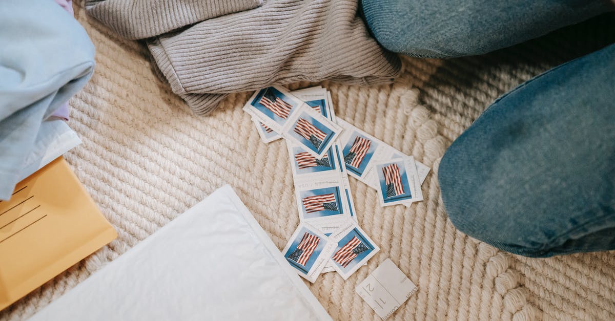 Flying to Scotland from the US, where do we check in? - From above crop anonymous person in jeans sitting on carpet on floor near heaped US postage stamps and envelope