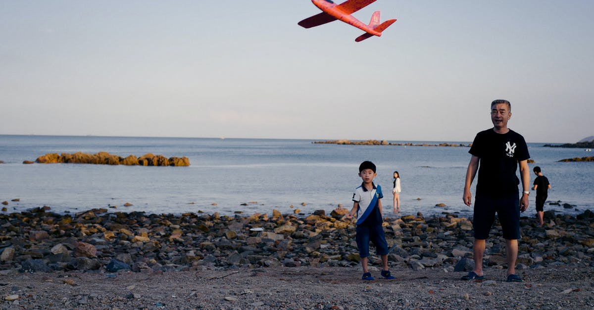 Flying with a lap child on a code shared flight - Ethnic father and son launching toy plane on beach at sunset