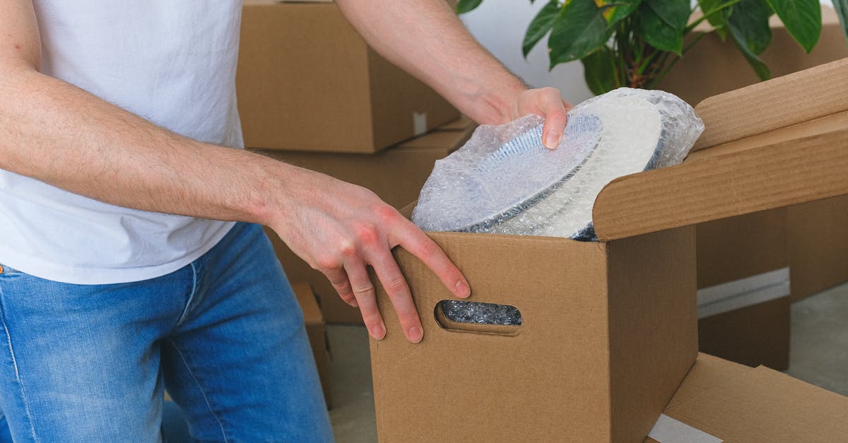 Flying with fragile items on KLM - Crop anonymous male in casual clothes packing fragile plates in carton box before moving into new flat in daylight