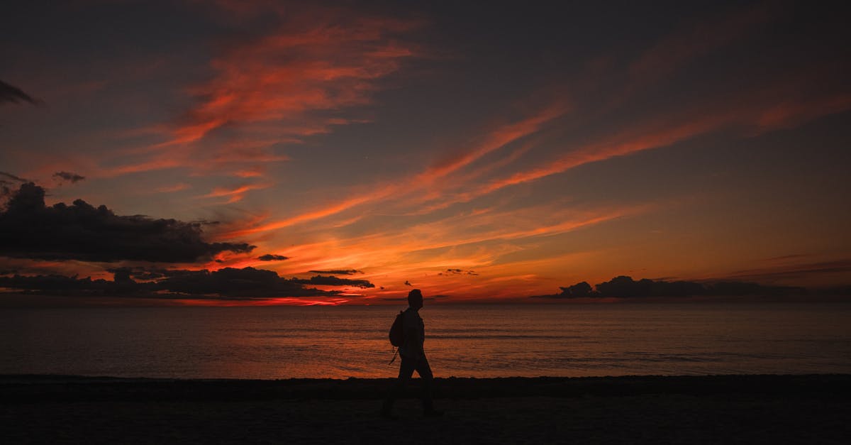 Forearm walking crutch and air travel - Anonymous backpacker silhouette walking on sea shore under sunset sky