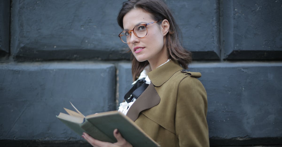 Forgot old passport with schengen/student visa - From below confident young female in glasses and elegant vintage clothes looking away and contemplating while reading rook on street near black wall of aged building in city