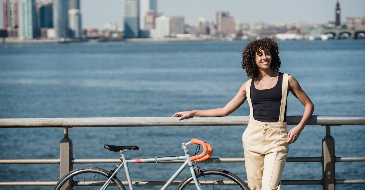 Found a lonely bike in Germany, what to do? [closed] - Young stylish ethnic female in trendy outfit standing with bicycle on embankment near river and city on background while looking away on sunny summer day