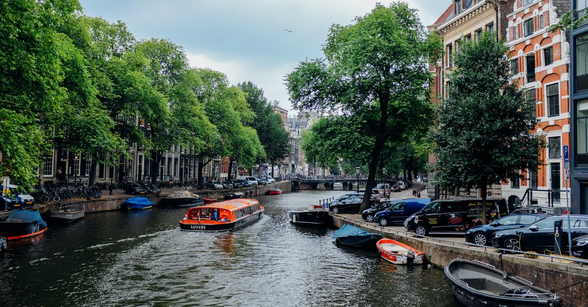 Four trip discount on Netherlands trains? - Picturesque scenery of modern vessel floating on calm channel with moored traditional boats amidst beautiful historic buildings and green trees in Amsterdam