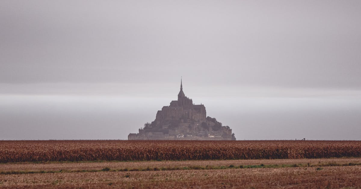 France visa processing time in Dubai per nationality - Scenery of distant grand Mon Saint Michel Abbey situated on vast grassy valley under cloudy gloomy sky