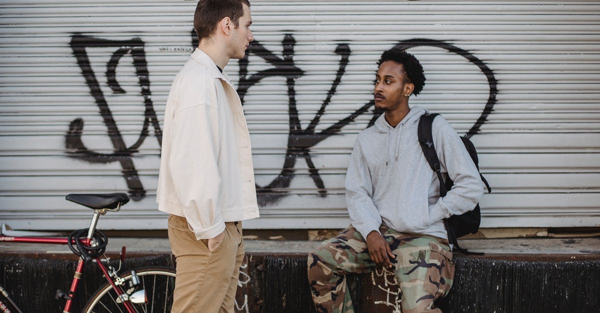 Free street parking in Montreal - Serious young multiracial male friends spending time together on city street near aged building with graffiti after riding bicycle