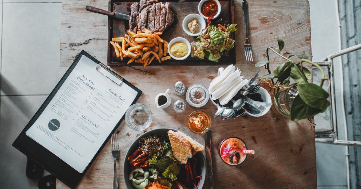 French Autoroute tolls - Top view of wooden table with salad bowl and fresh drink arranged with tray of appetizing steak and french fries near menu in cozy cafe