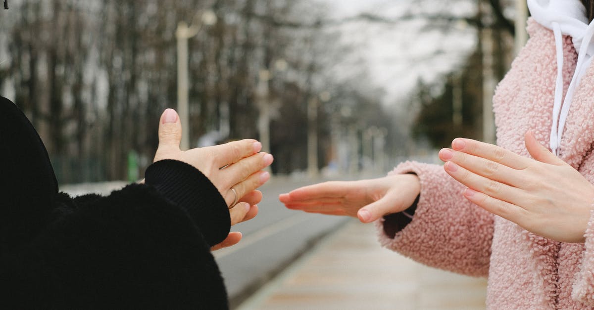 French street language in mugging situation - Crop anonymous people in outerwear standing in park on blurred background in winter and using sign language