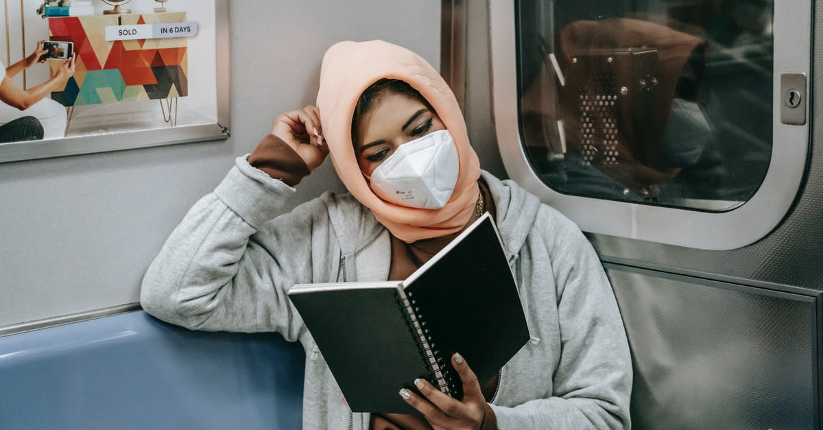 Frequent short-term student visa - UK/US citizen - Faceless young Muslim ethnic woman in casual outfit and hijab with protective mask reading notebook while sitting in train in metro