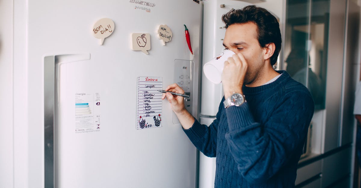 Fridge magnets in San Francisco! - Young man writing reminder on fridge and drinking coffee at home