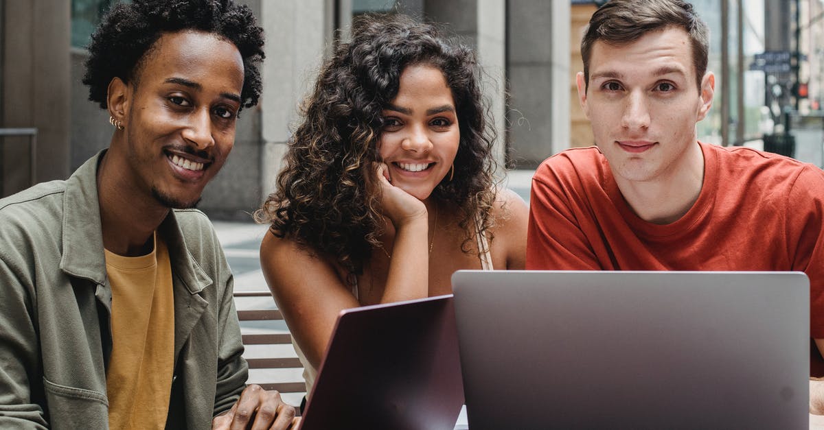 Friend needs help in Turkey - Young multiethnic friends in casual outfit using netbook while sitting at table in city street and looking at camera