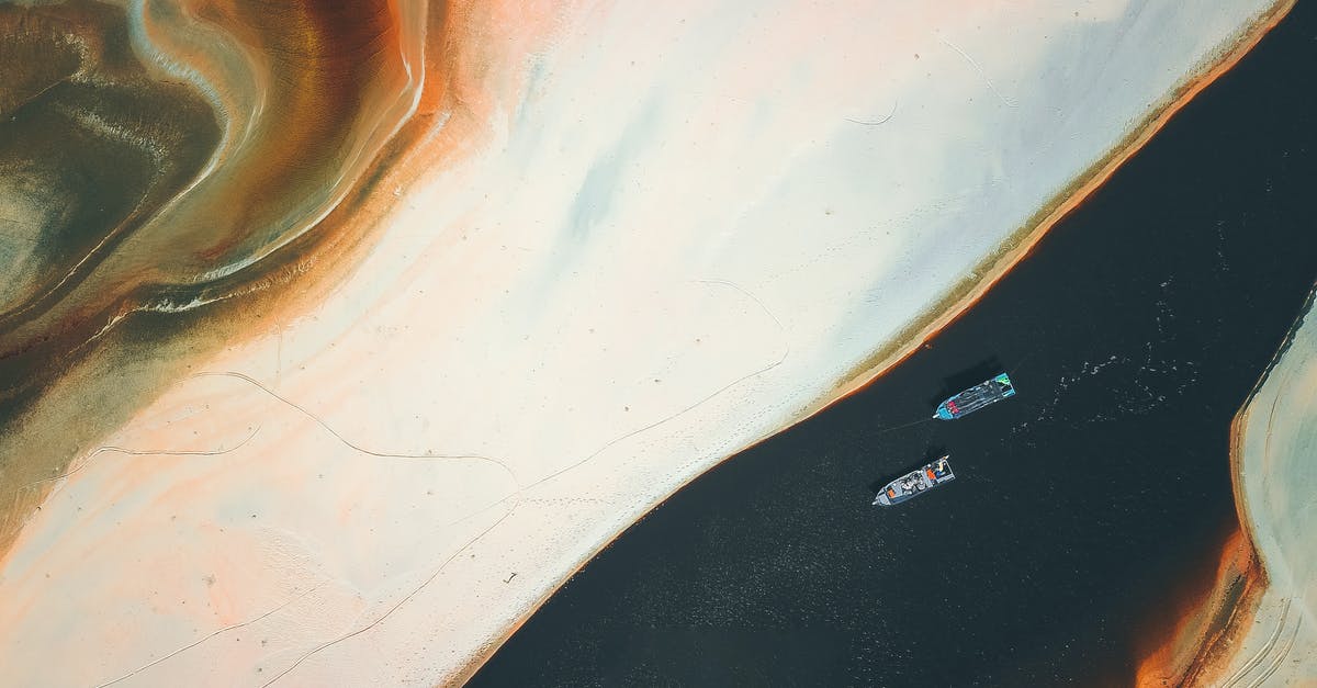 From France west coast to Portugal via ship? - Aerial view of colorful textured sandy shore near floating boats in water in sunny day