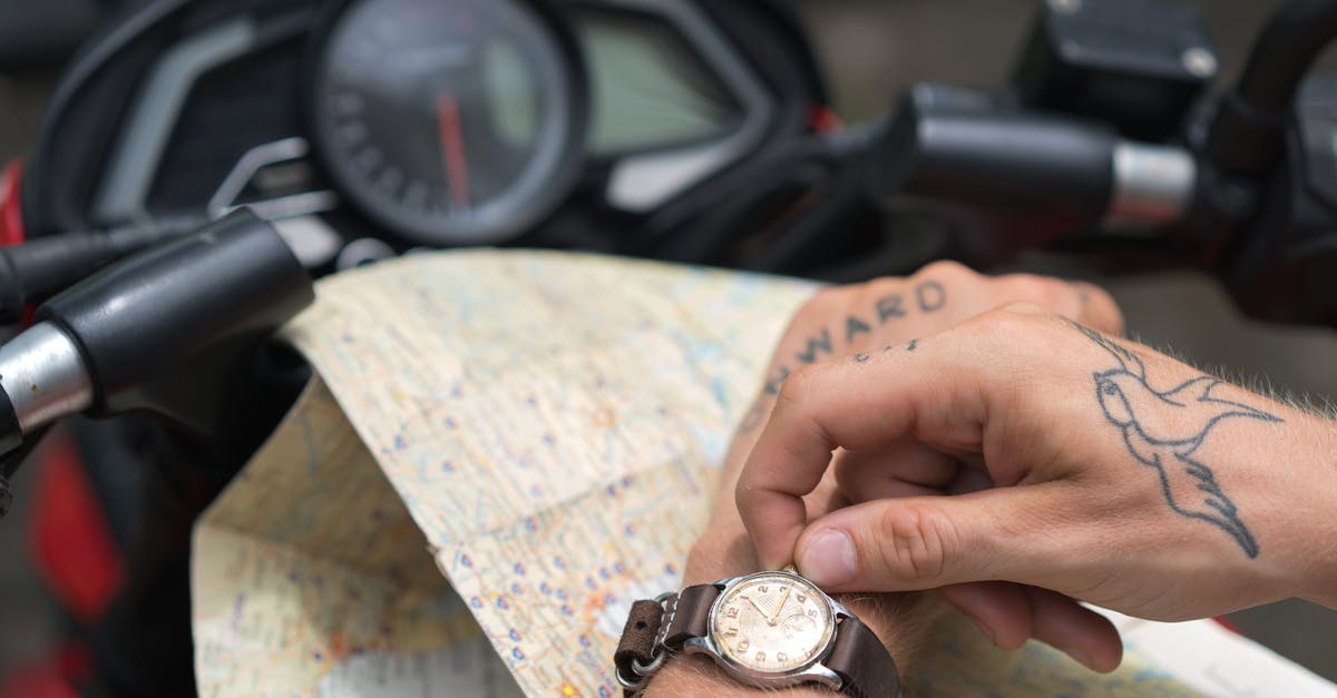 From JFK to Newark. Time & transportation alternatives - Crop tattooed man setting up watch against map and motorbike