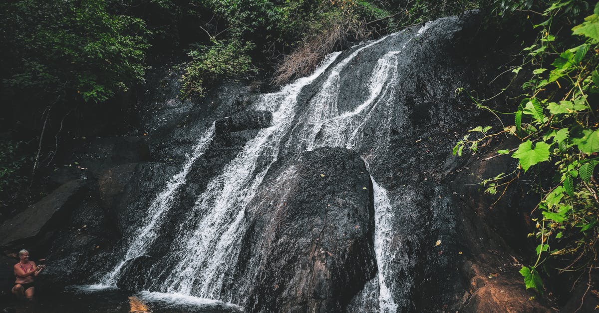 From Puno to La Paz through Lake Titicaca? - Unrecognizable travelers chilling in warm pond formed by waterfall flowing through rough stony cliff in lush forest