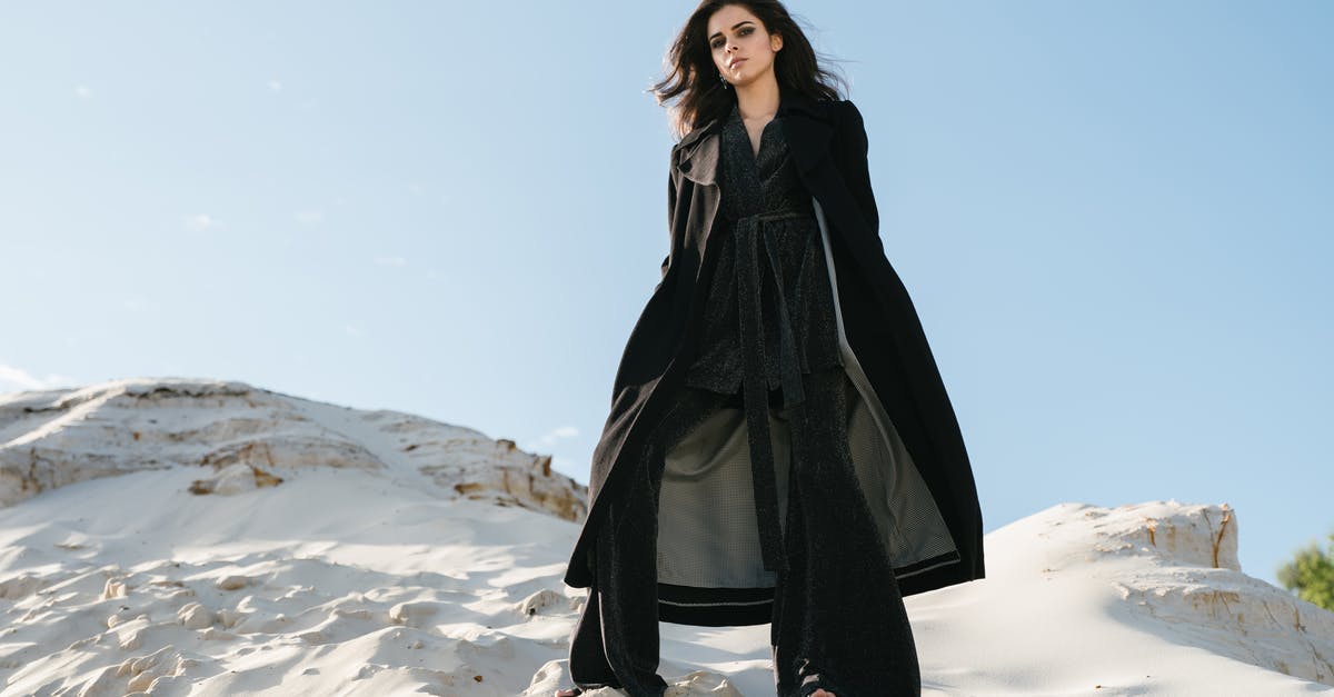 From UK to Chile through Atlanta [duplicate] - From below full length young pensive good looking brunette in trendy black outerwear with hands in pocket standing on sandy cliff against blue cloudless sky and looking at camera