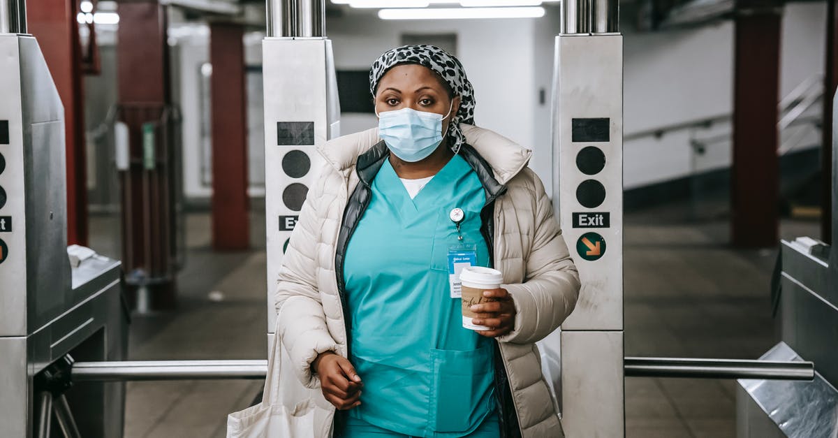 Gate pass at ORD to meet teenager (non-Unaccompanied Minor) - Calm adult African American nurse with coffee to go wearing warm outfit and protective face mask passing through turnstile in metro station and looking at camera