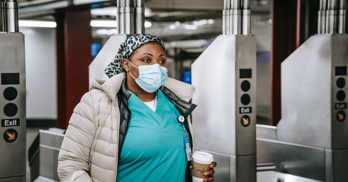 Gate pass at ORD to meet teenager (non-Unaccompanied Minor) - Black nurse in outerwear and mask passing turnstile in underground