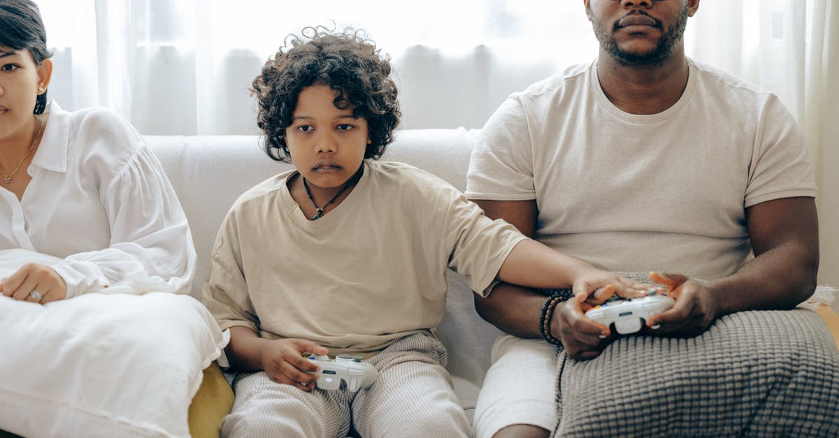 Gate to gate electronic device usage on AmericanConnection/Chautauqua Airlines? - Concentrated child showing usage of gamepad to father while playing on game console and resting on sofa together with family