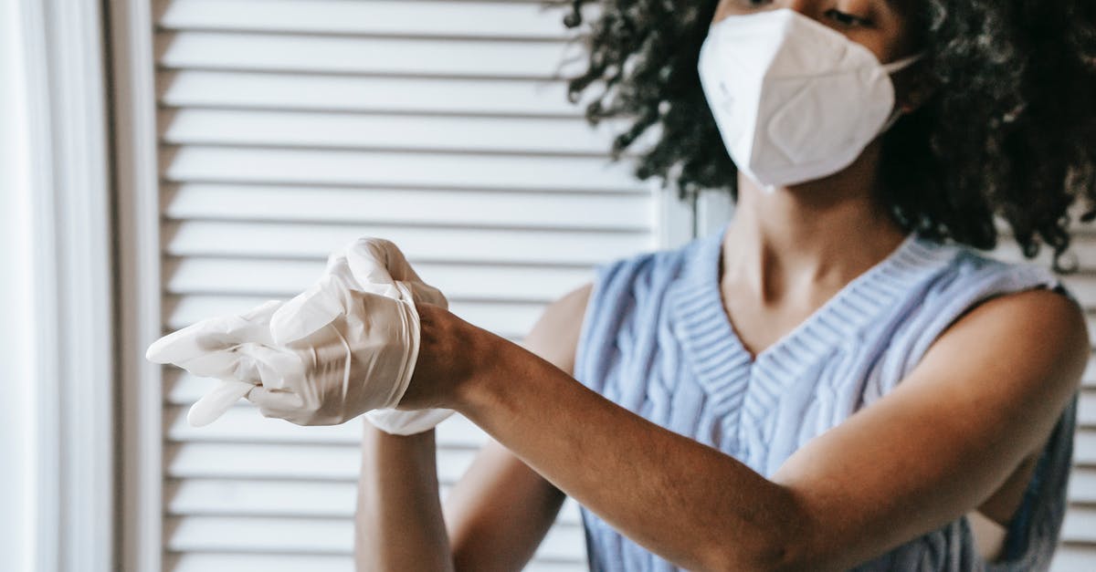 Germany Layover Covid Restrictions - Young African American female in white protective face mask putting of medical latex gloves