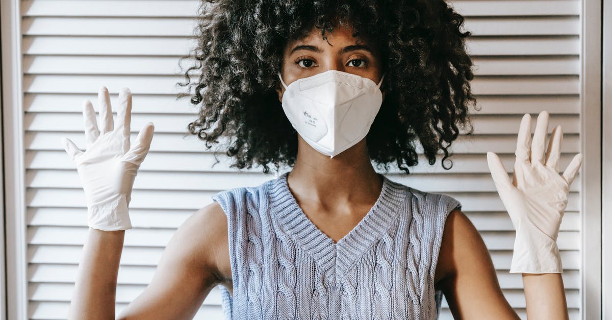 Germany Layover Covid Restrictions - Young African American female wearing white protective face mask and medical white rubber gloves with hands raised looking at camera