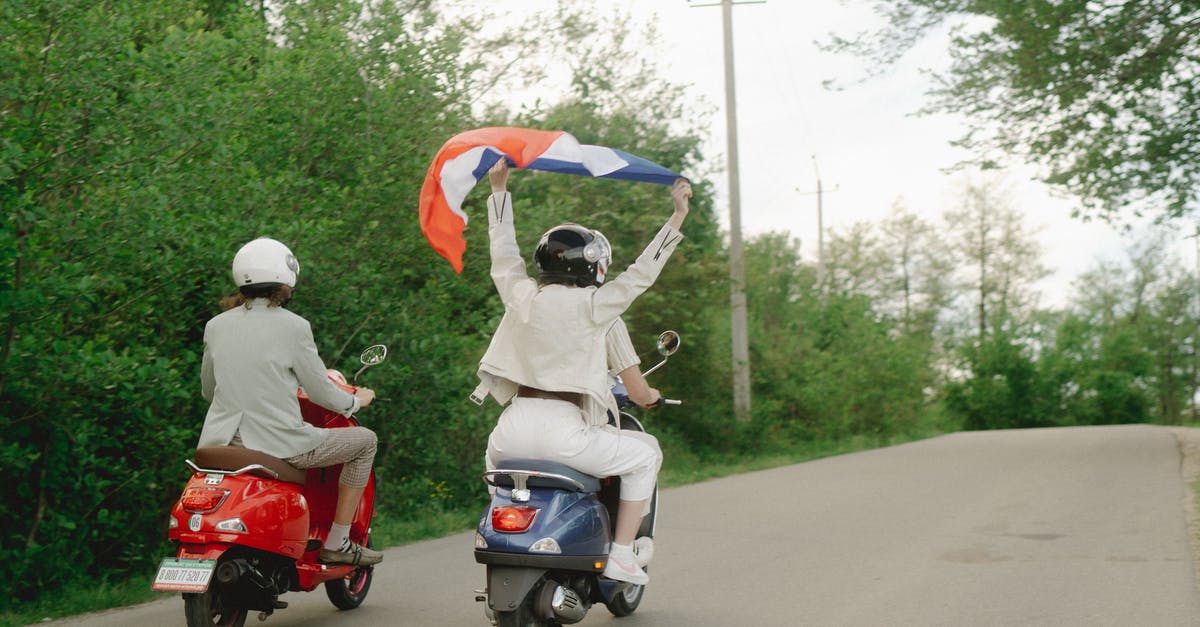 Getting a motorcycle license in France - People Riding a Motor Scooters on the Road while Holding a Flag