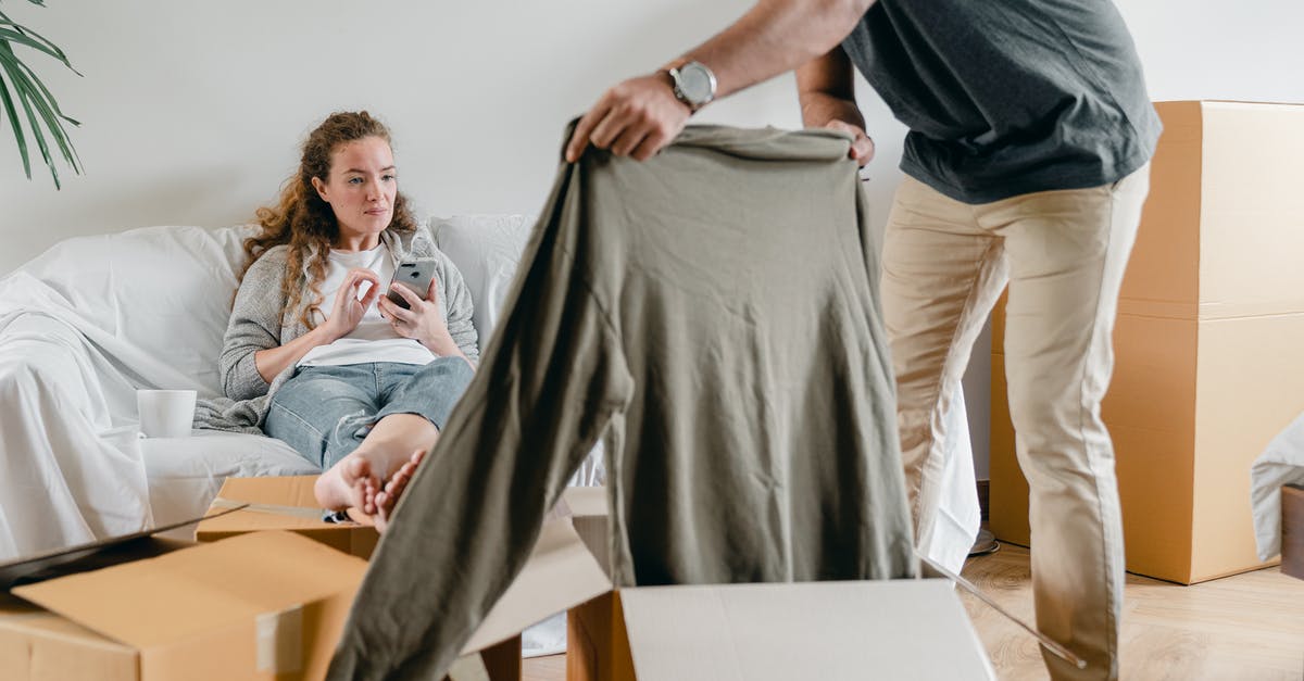 Getting a UK visitor visa for my girlfriend - Crop anonymous male in watch getting polo neck out of cardboard box while standing near pensive barefoot girlfriend sitting with crossed legs on comfortable couch after moving into new flat