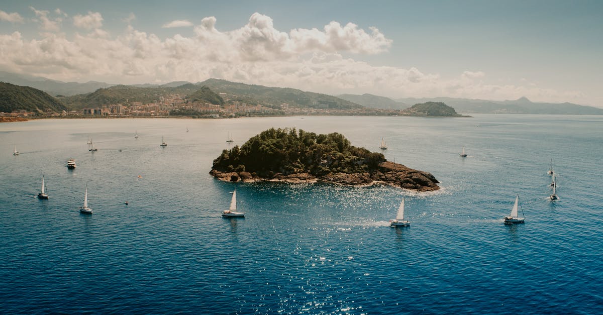 Getting around Cape Verde islands from Sal - Picturesque seascape of sailboats floating around little island in blue rippling water near hilly coast under cloudy blue sky