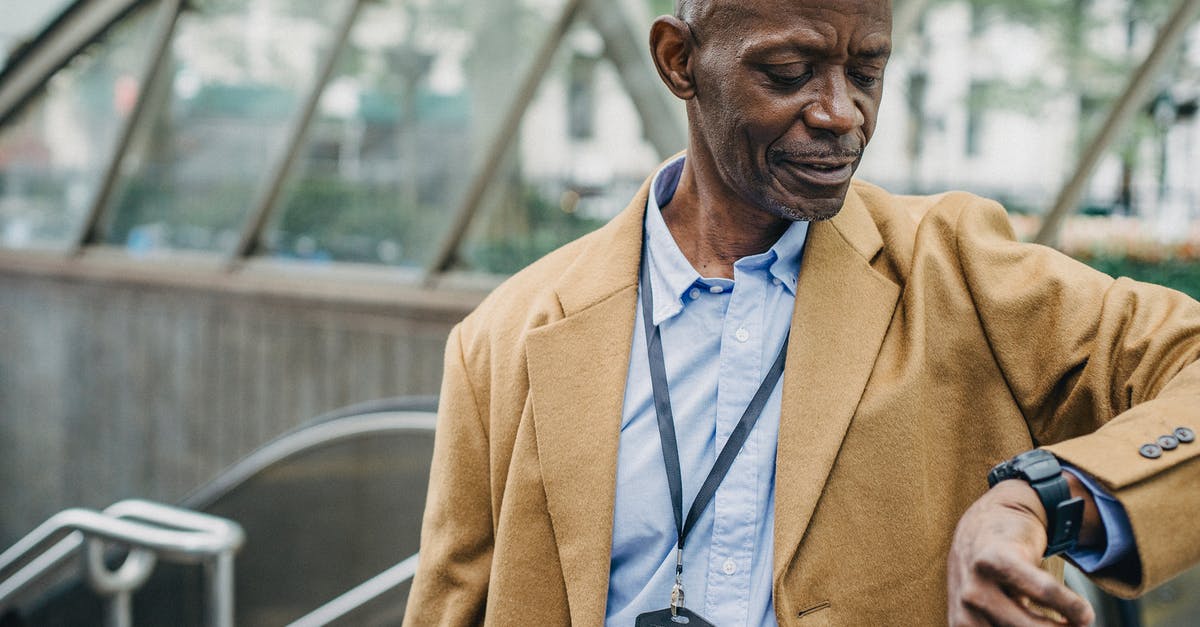 Getting from SFO to Berkeley during rush hour - Crop punctual African American male in elegant formal clothes standing near metro entrance and checking time on wristwatch