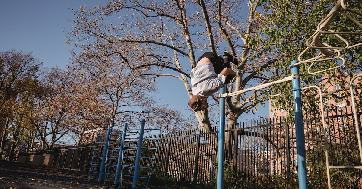 Getting from Victoria Falls airport to town - From below full body of unrecognizable male doing parkour while backflip in park near metal turnstile in street in sunny autumn day near trees with fence under blue cloudless sky