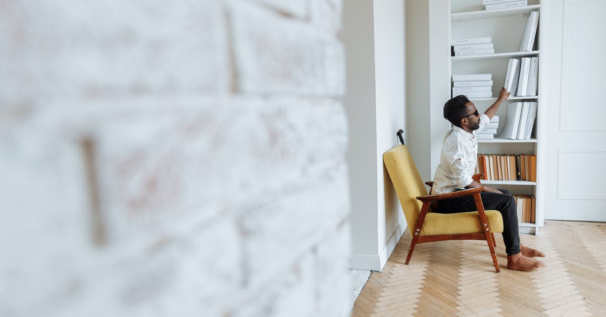 Getting into a fully booked hotel? - A Man Sitting on a Chair and Getting a Book on the Shelves