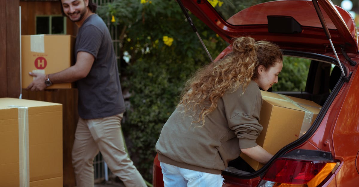 Getting my Filipino boyfriend a UK visa - Young woman with curly hair getting carton box out from trunk of automobile while cheerful ethnic man carrying box into new home in suburb or countryside area