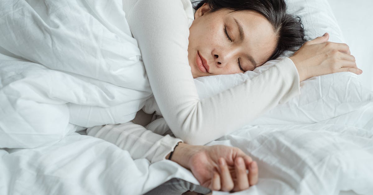 Getting to Kazan (RU) Airport early in the morning - Calm Asian female wearing white pajama sleeping in comfortable bed with white sheets near modern mobile phone in morning