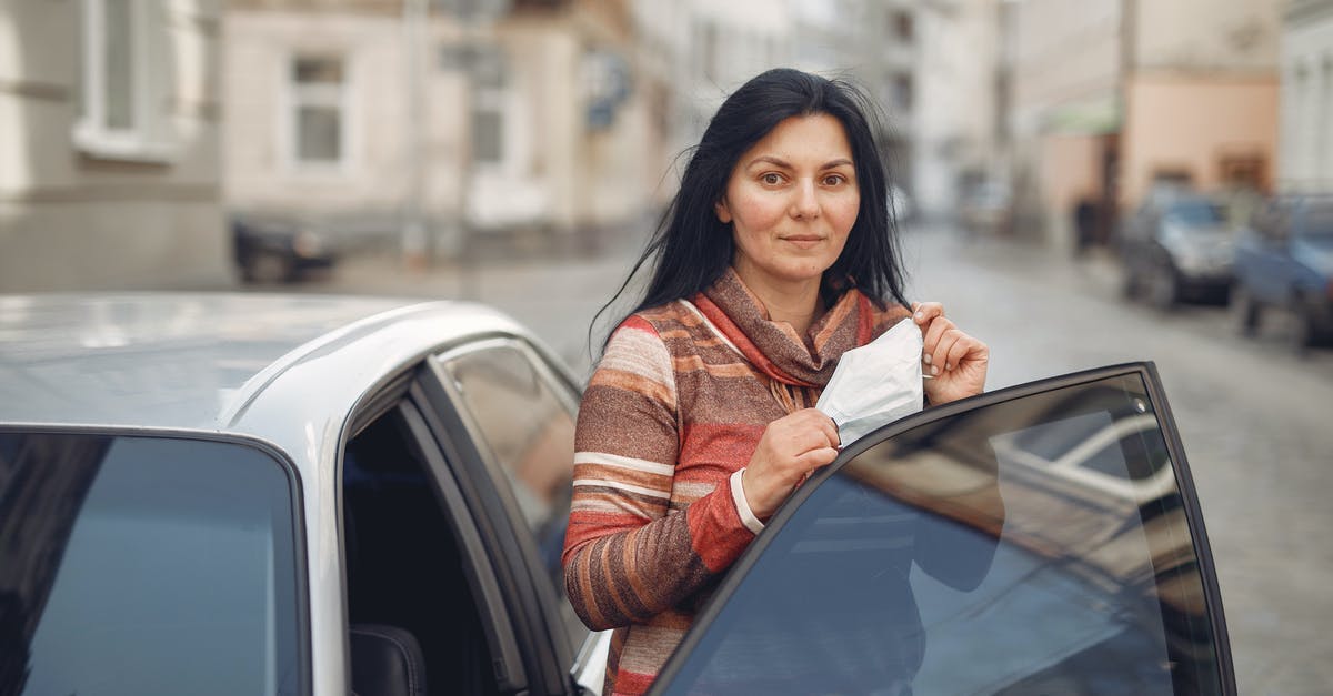 Getting TSA precheck with Global Entry - Content young woman with medical mask in hands standing near car on urban street