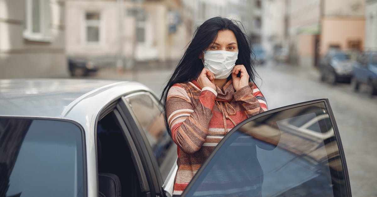 Getting TSA precheck with Global Entry - Young woman wearing medical mask standing near automobile on empty urban street