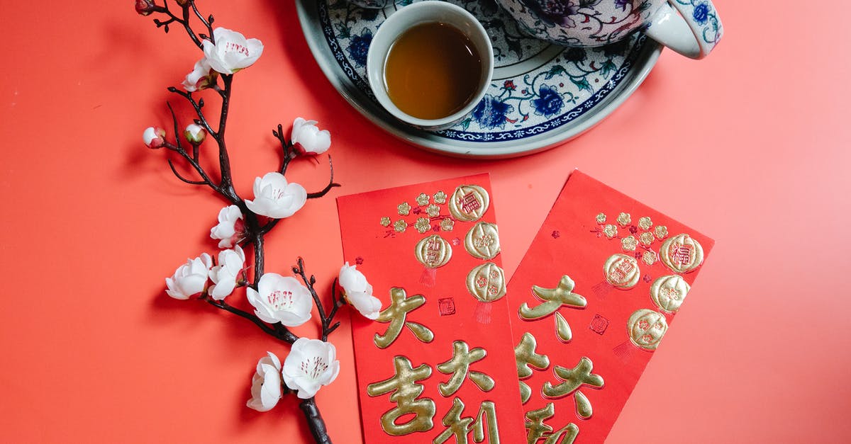 Gifts for Chinese hosts? - Top view of oriental packets with hieroglyphs against blossoming flower sprig and tea set during New Year holiday on red background