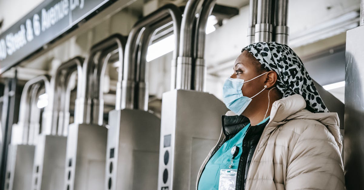 Going from London Heathrow/LHR T5 (arrivals) to T2 (arrivals) - Side view emotionless African American female doctor wearing warm clothes and protective face mask passing through turnstile gates in New York underground