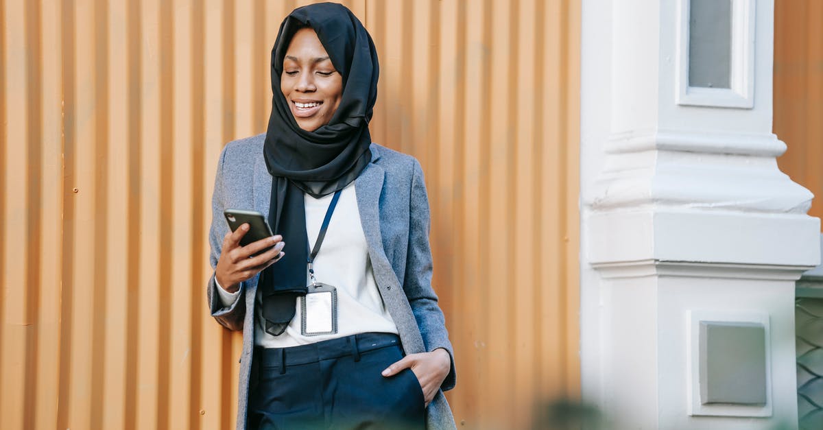 Good and stable internet in Mexico - Cheerful young African American female entrepreneur in classy outfit and Islamic headscarf smiling while reading good news on smartphone and standing near building on street