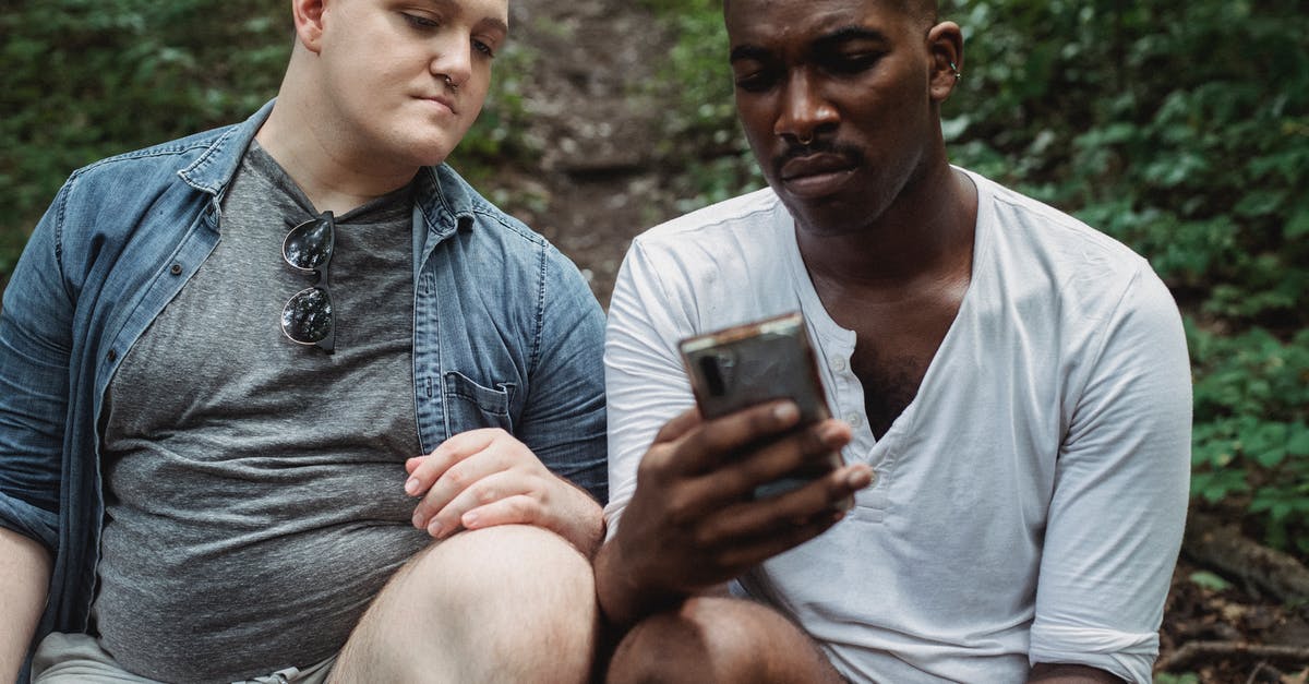 GPS coordinate problem - Concentrated multiethnic male travelers surfing internet while relaxing in woodland in daytime on blurred background