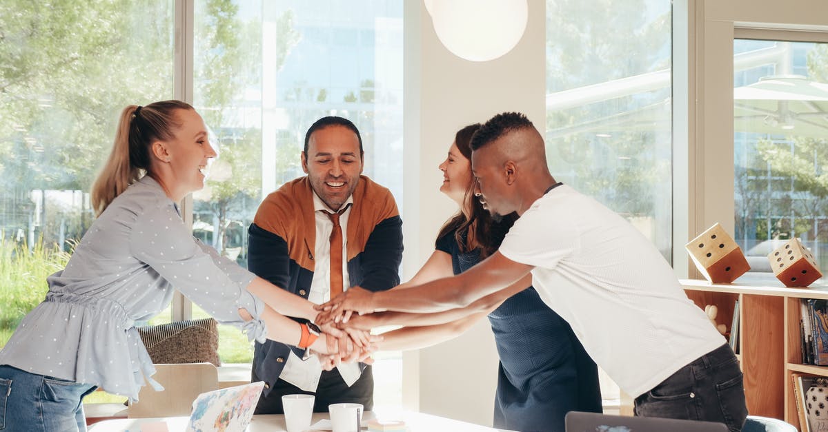 Group visa applied but not received for one member - Content multiethnic colleagues joining hands above table with laptops in modern office on sunny day