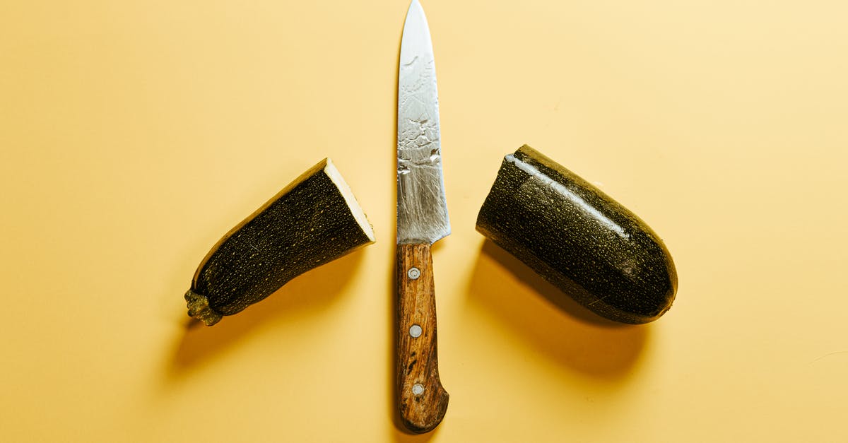 Half an hour layover in Vienna between international flights - From above of fresh sliced zucchini placed on yellow background with sharp knife with wooden handle between halves of vegetable