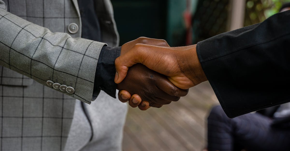 Handshake while holding own right elbow - Men in Suit Jackets Shaking Hands