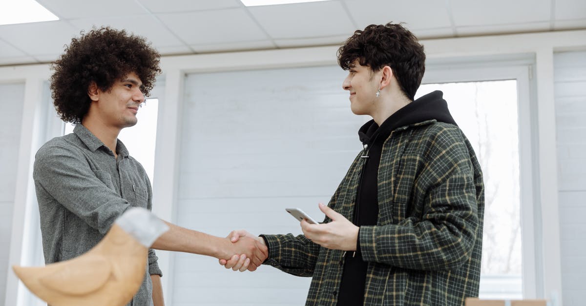 Handshake while holding own right elbow - A Man Holding a Smartphone Shaking Hands with a Man in Gray Shirt