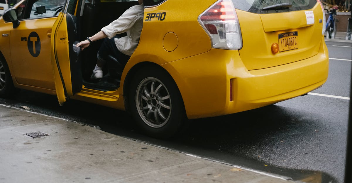 Hanoi: 1.8 million VND taxi fare? [closed] - Unrecognizable passenger closing door of yellow cab with logo and headlight parked on asphalt road near pavement on street in city