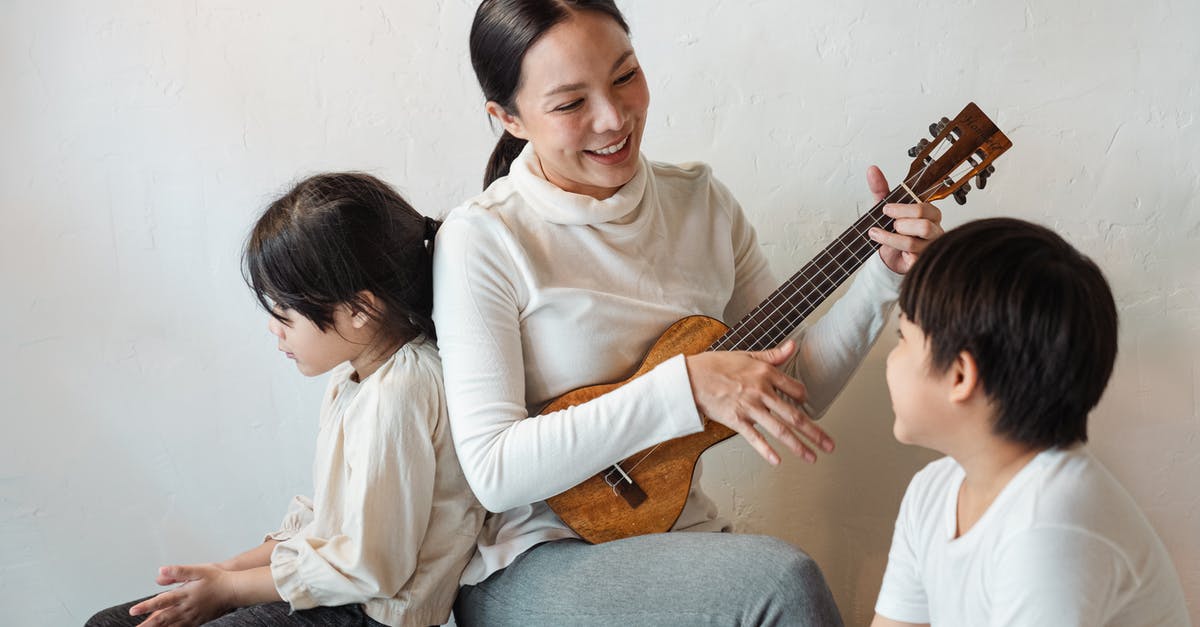 Hawaiian Airlines Boarding/Deboarding Music - Happy musician sitting with crossed legs while playing traditional Hawaiian musical instrument for happy unrecognizable ethnic son and pensive anonymous daughter sitting on wooden bench at home